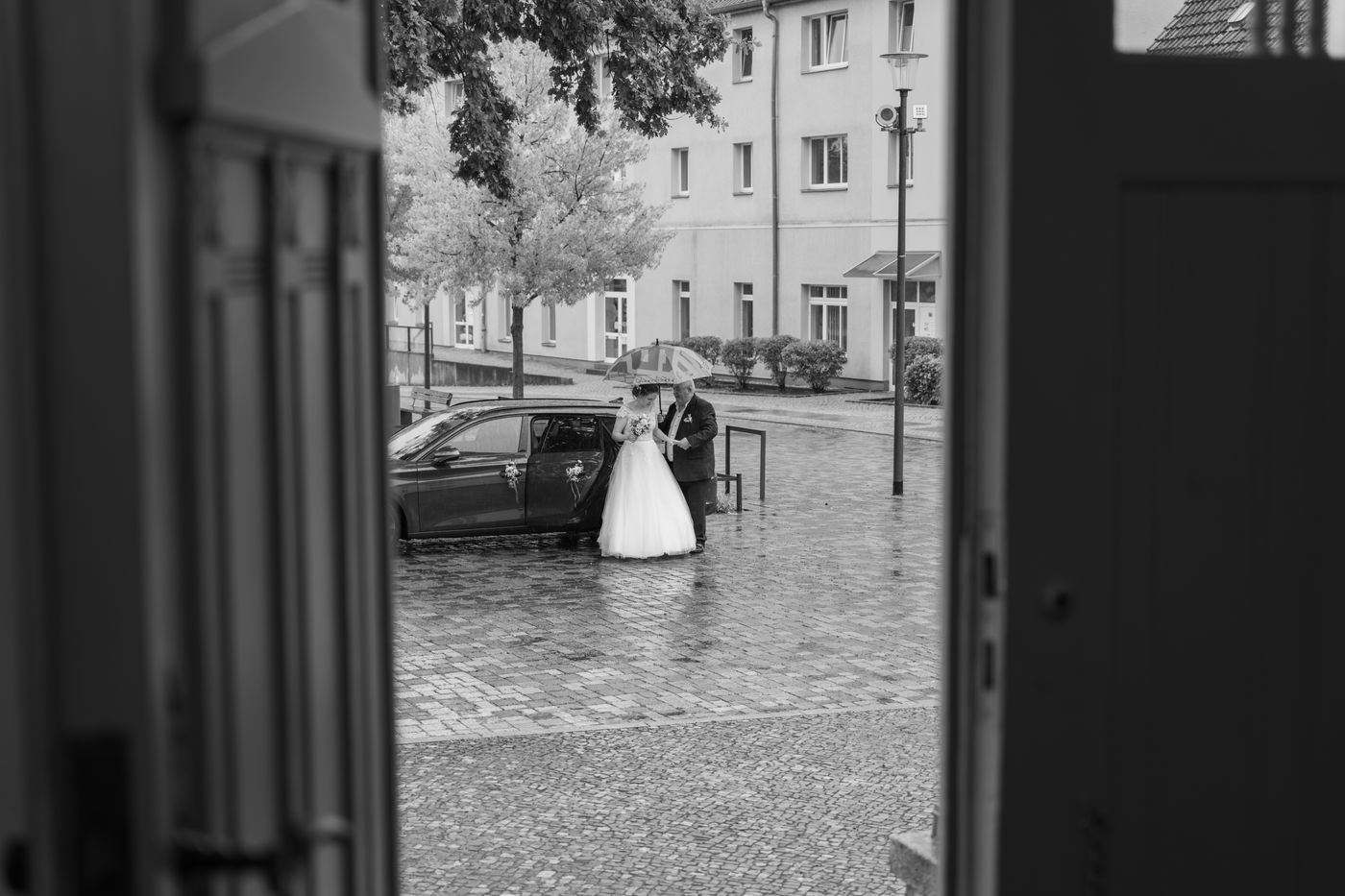 Brautpaar im Regen, durch eine Tür fotografiert – Hochzeitsfotografin Elisa, Berlin & Brandenburg